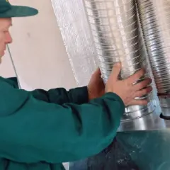 Instalator montuje rury do rozprowadzenia ciepłego powietrza z kominka.