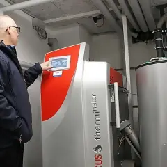 Mężczyzna obsługuje nowoczesny piec na pellet do salonu. Urządzenie z panelem dotykowym i dużym zasobnikiem zapewnia komfortowe ogrzewanie.