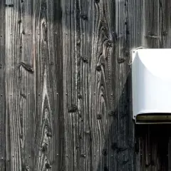 Biały dolot powietrza do kominka na ciemnej, drewnianej elewacji.
