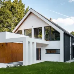 Nowoczesny, biało-czarny dom z drewnianą bramą garażową, otoczony zielenią.