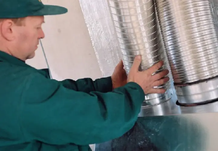 Instalator montuje rury do rozprowadzenia ciepłego powietrza z kominka.