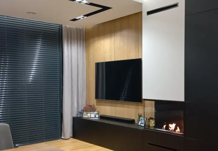 Nowoczesny salon z telewizorem i palącym się kominkiem bio do zabudowy.