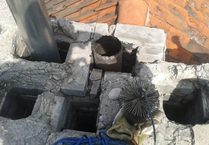 Widok na zniszczony komin z rurą i szczotką do czyszczenia. Widać fragmenty cegieł i dachówki. To miejsce, gdzie mógłby być zamontowany kominowy wymiennik ciepła.