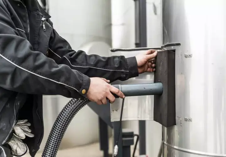 Pracownik czyści komin przez drzwi wyczystki kominowej, używając węża.