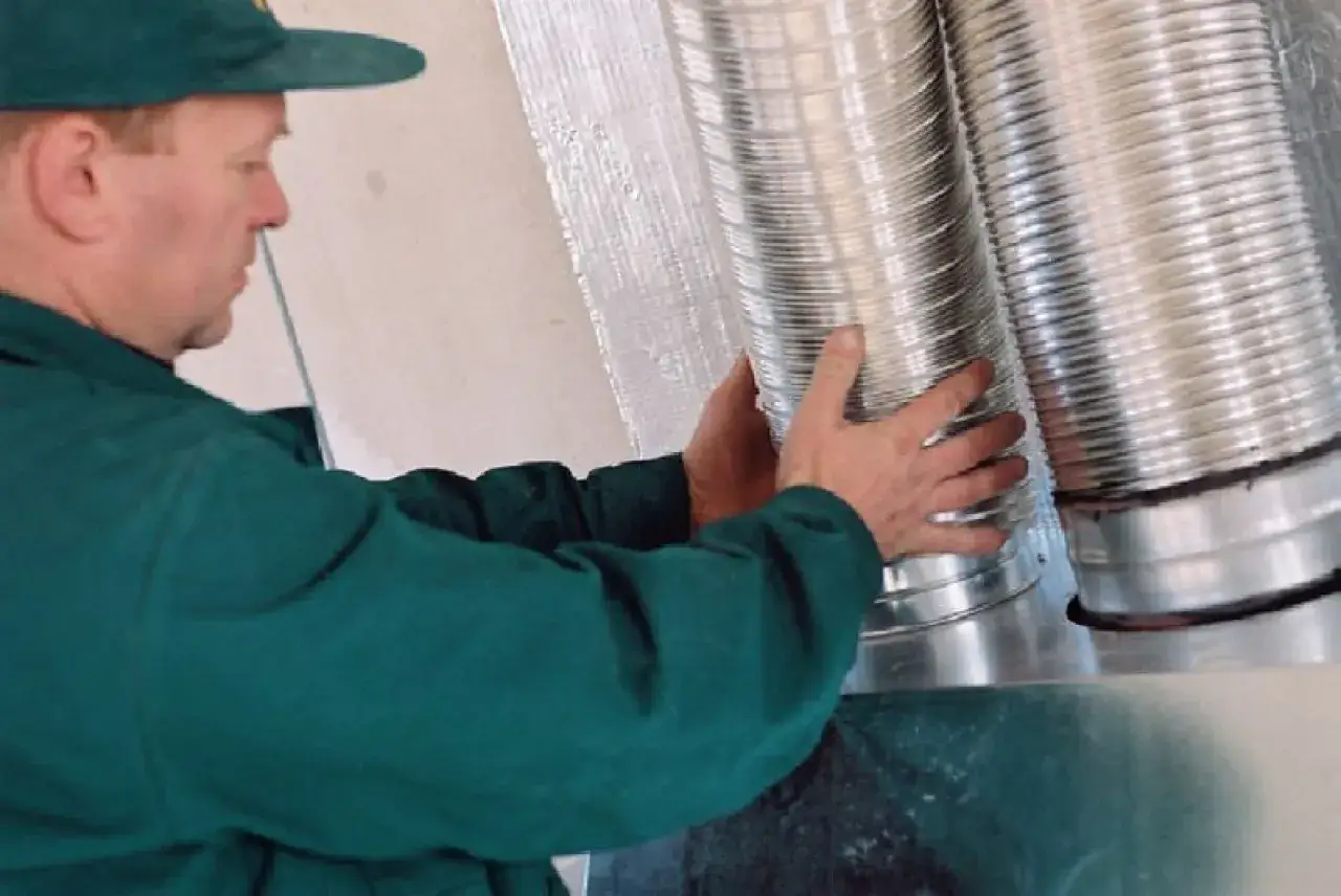 Instalator montuje rury do rozprowadzenia ciepłego powietrza z kominka.